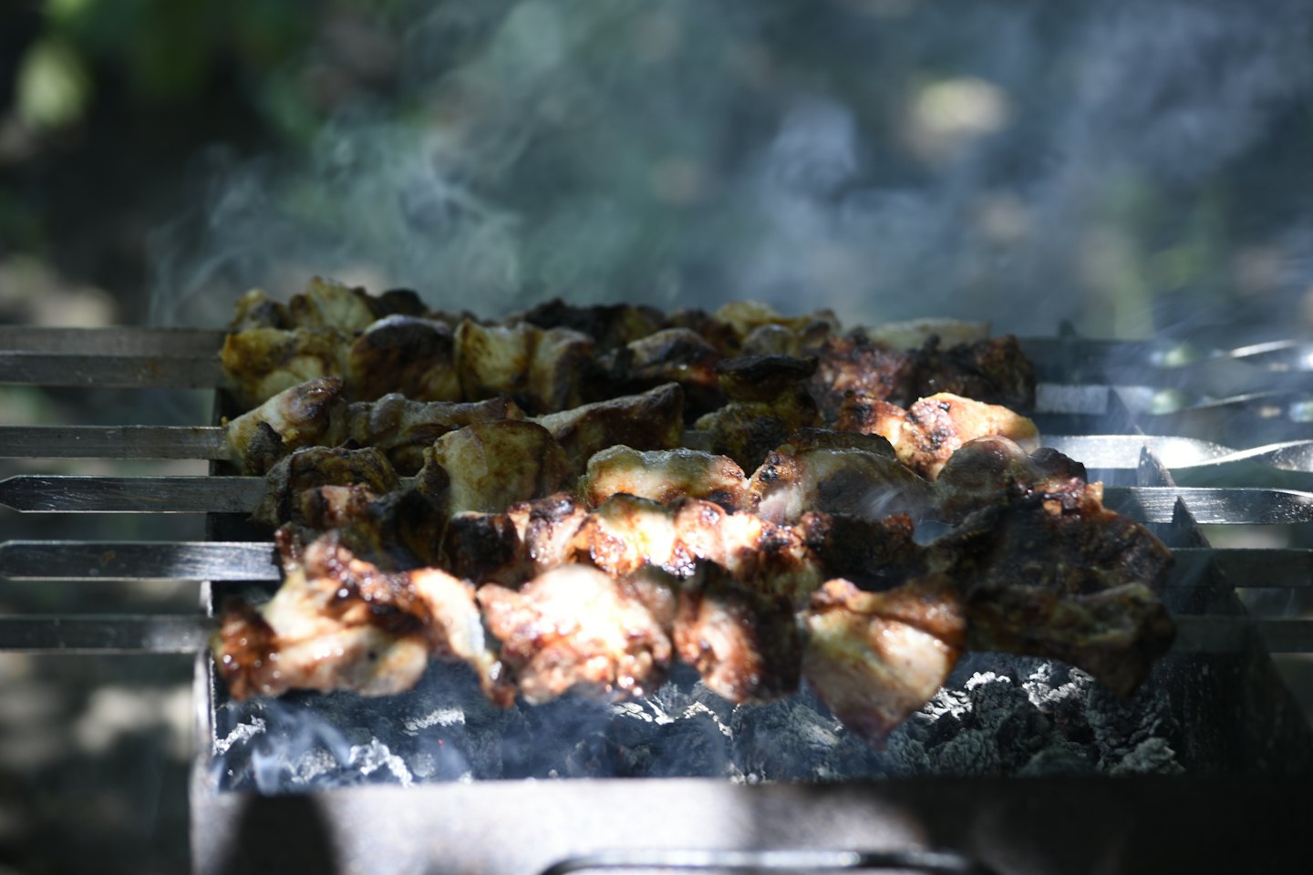 Meat skewers cook over glowing coals on a backyard grill.