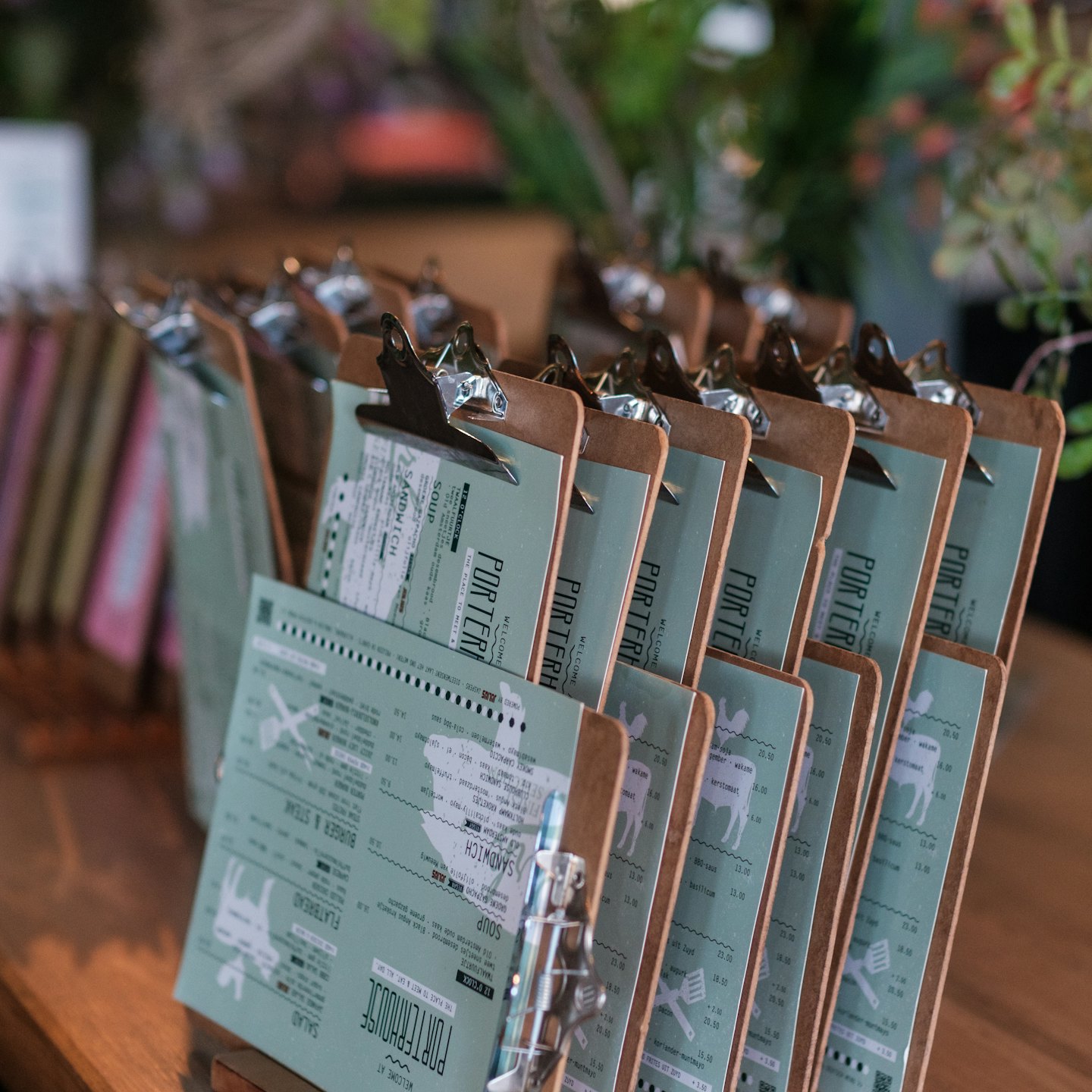 Green restaurant menus on clipboards stand on a wooden table.