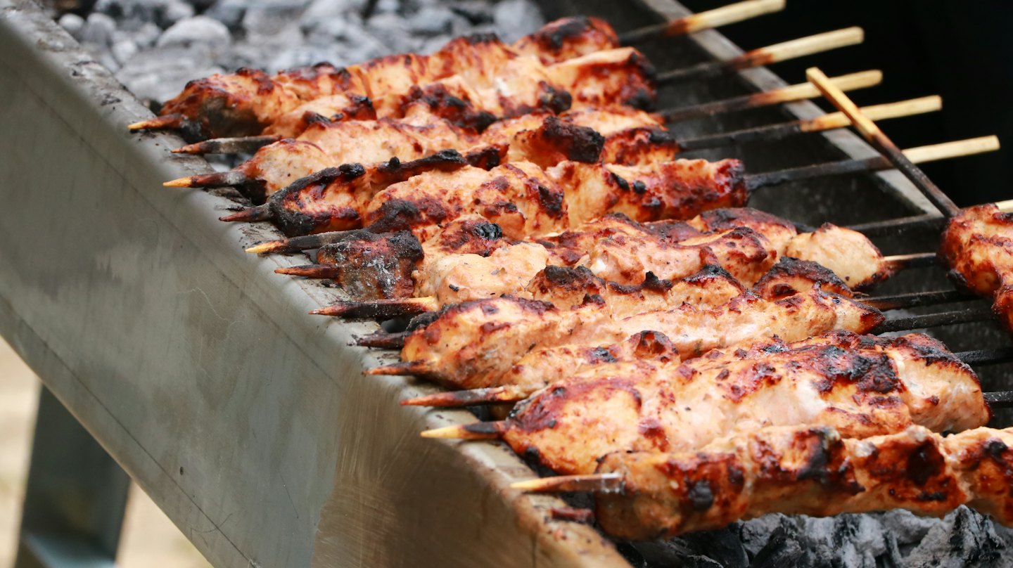 Marinated meat skewers grilling over hot charcoal on a barbecue.
