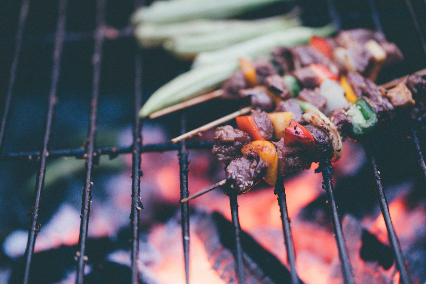 Beef and vegetable skewers grilling over hot coals.