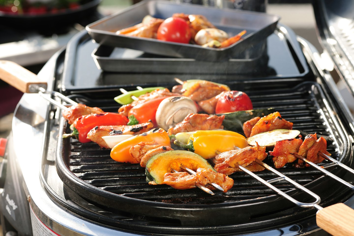 Colorful vegetable and chicken skewers grilling on an outdoor barbecue.