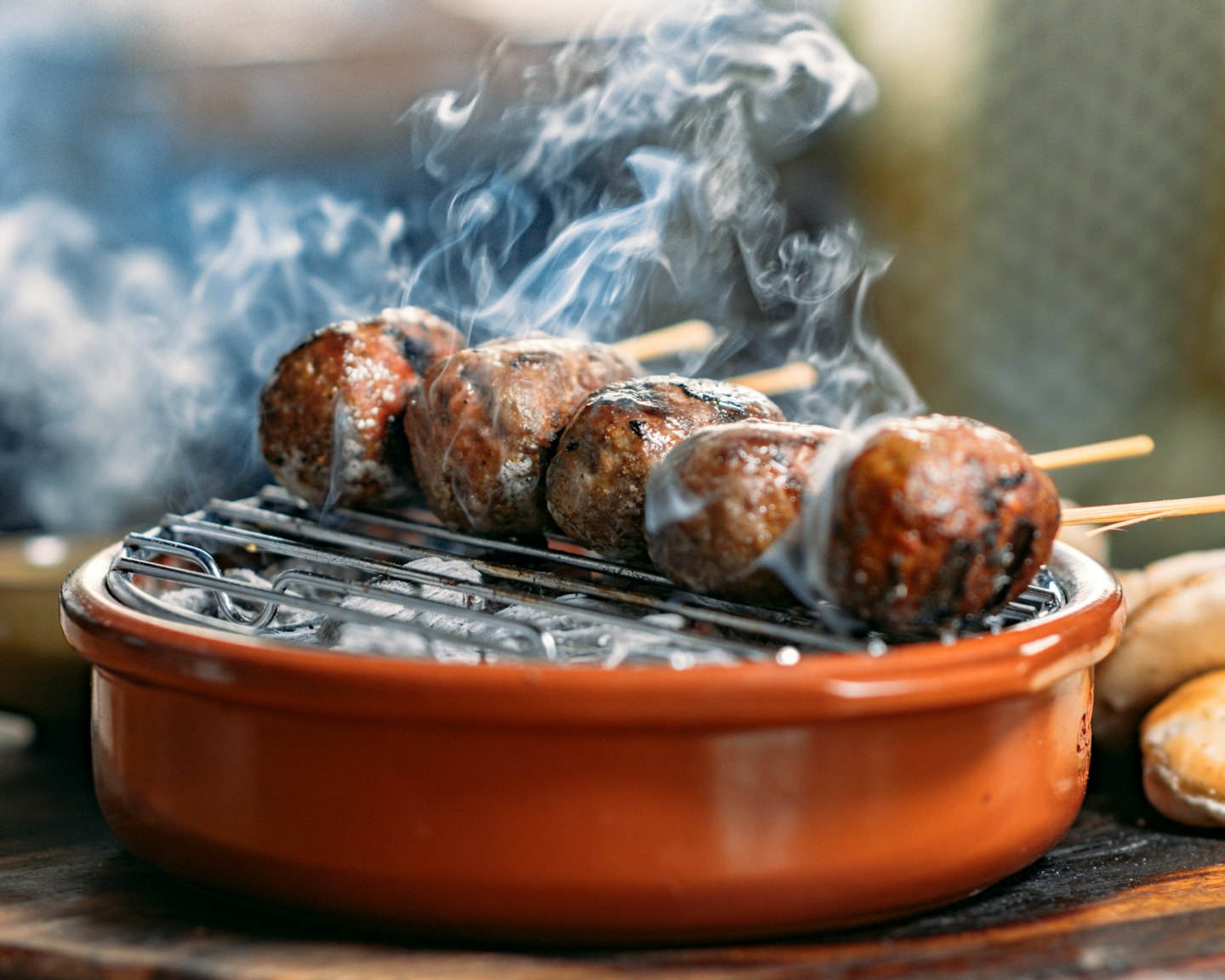 Grilled meatballs on wooden skewers sizzle over hot charcoal coals.